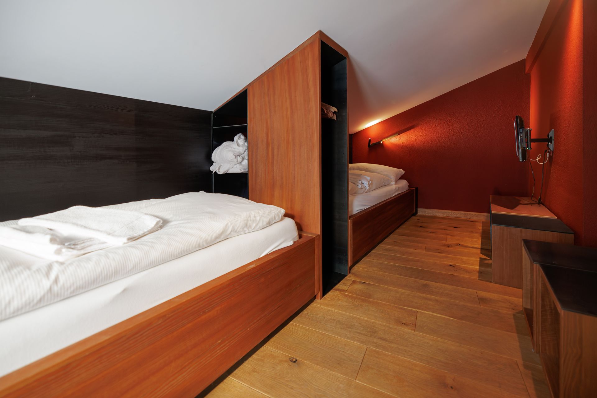 Modern hotel room with two beds, wood paneling, and red accent wall