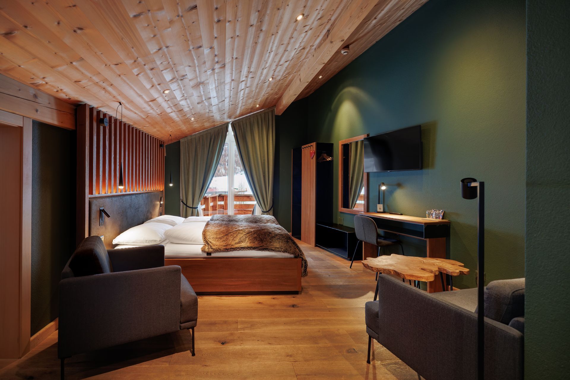 Modern bedroom with wood ceiling, green walls, bed, and seating area