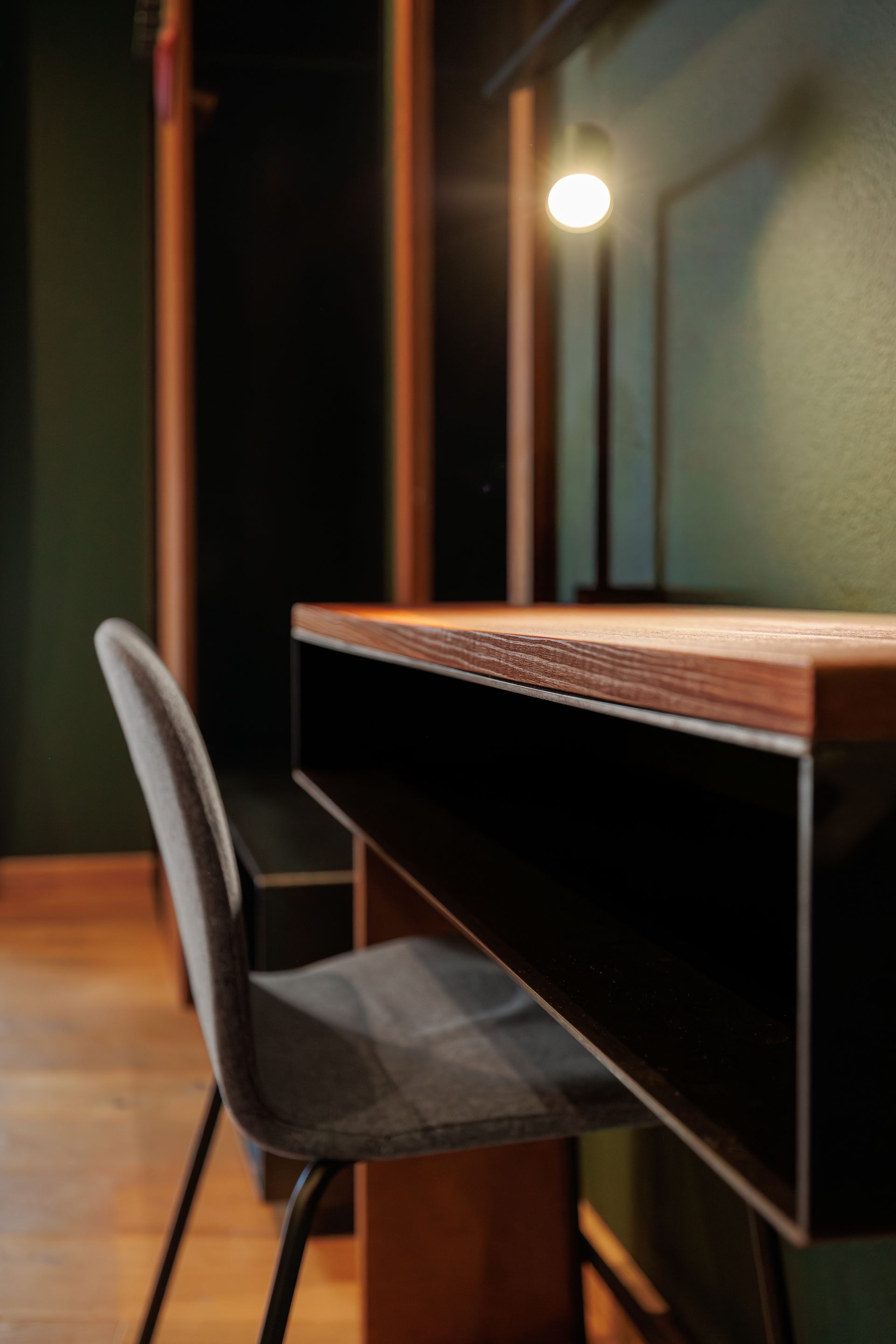 Modern desk with gray chair in a dimly lit room, warm lamp glowing nearby