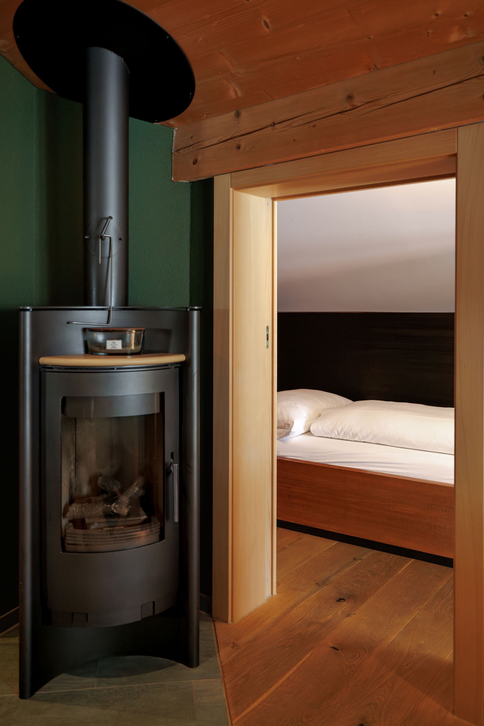 Modern cabin interior with a black wood stove beside a doorway to a cozy bed nook