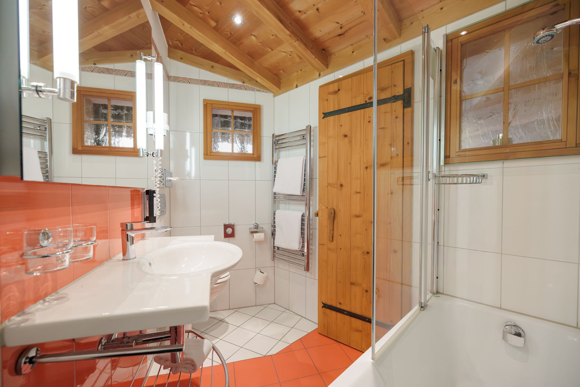 Small bathroom with wood-paneled ceiling, sink, shower, toilet, and bathtub in warm orange and white tones