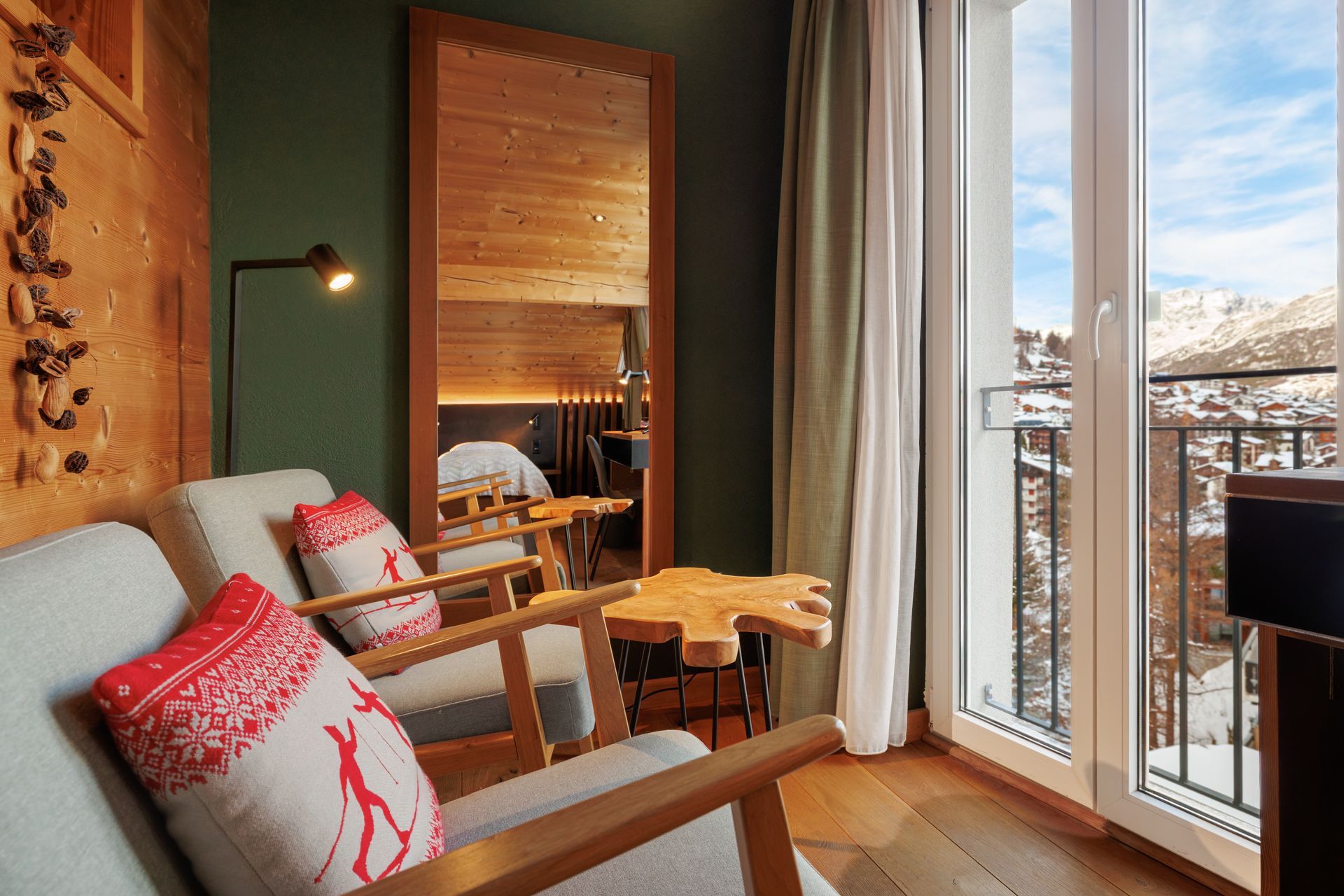 Cozy modern living room with sofa, wooden chairs, and floor-to-ceiling windows overlooking snowy mountains