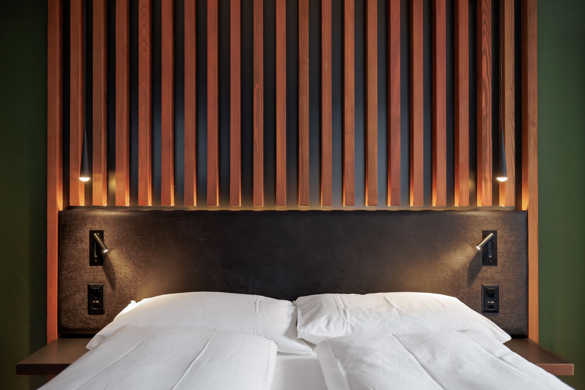 Modern hotel bedroom with white bedding, dark upholstered headboard, and vertical wood slats behind it
