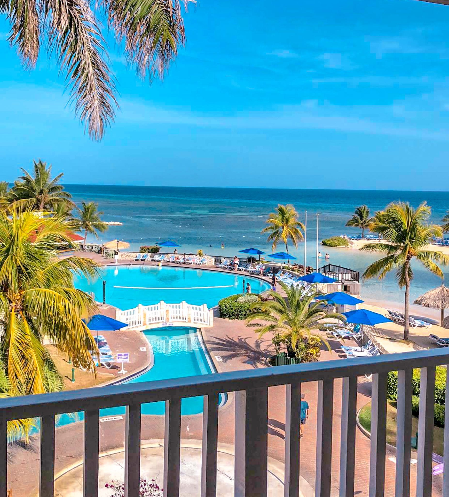Oceanfront resort with turquoise pool, palm trees, and beach view from a balcony