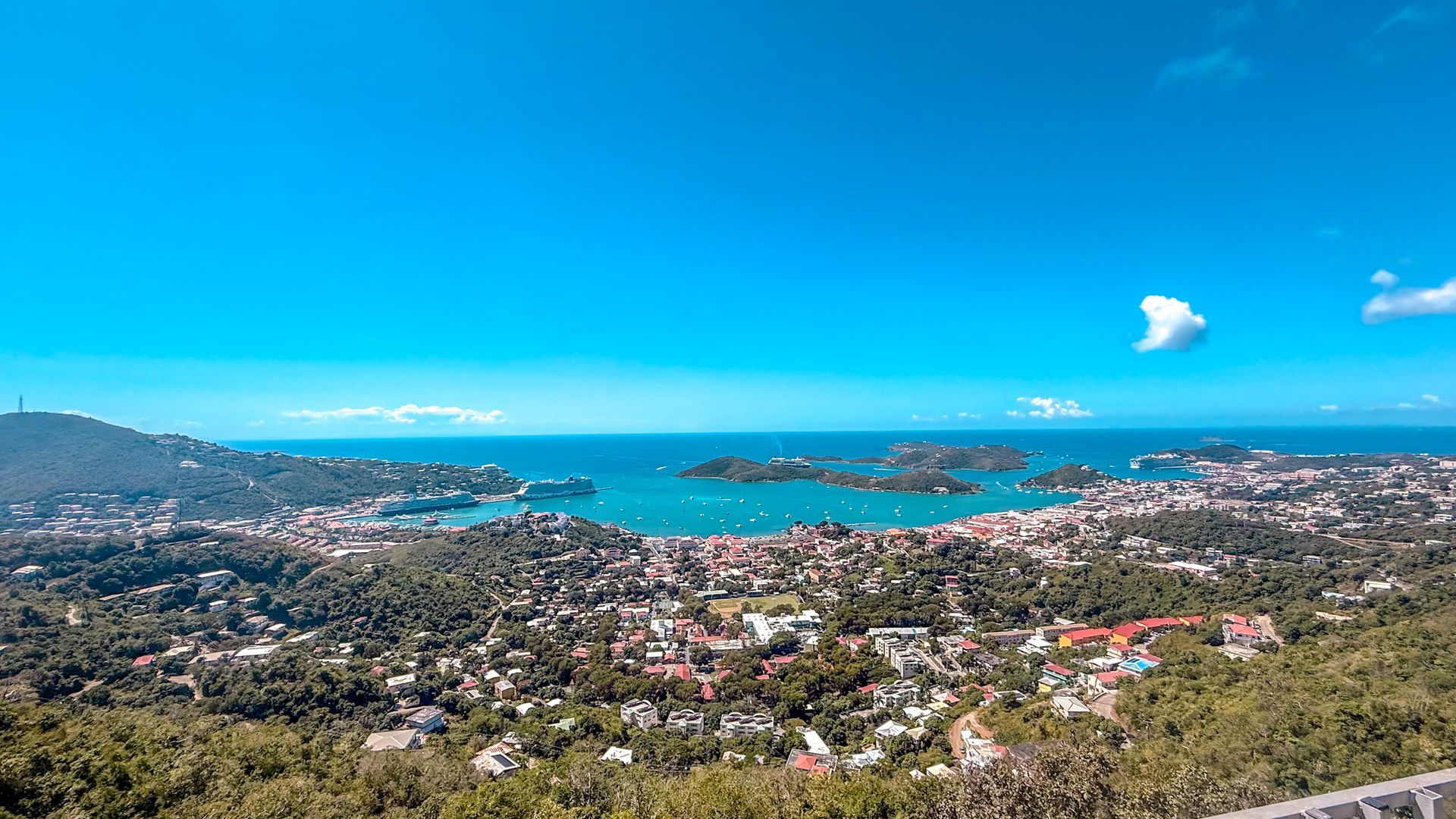Panoramic coastal city and bay under a bright blue sky with scattered clouds