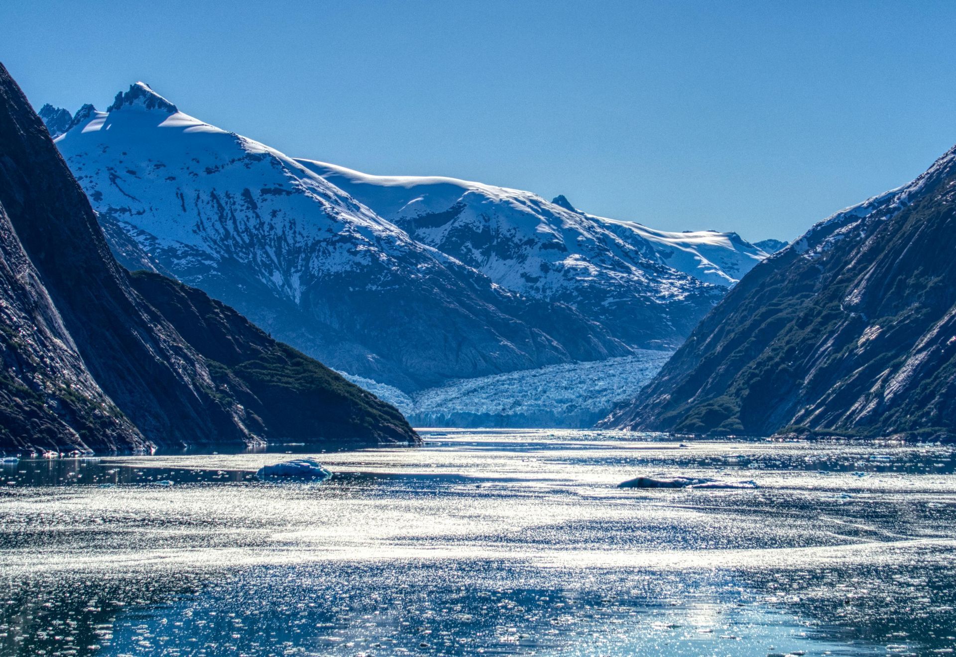 Snowy mountain fjord with sunlight reflecting on calm blue water
