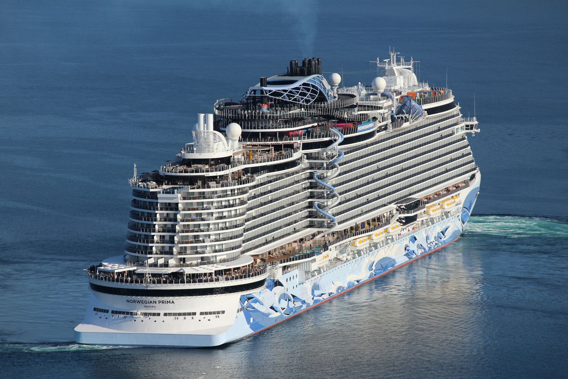 Large white cruise ship sailing on calm blue water, seen from above.