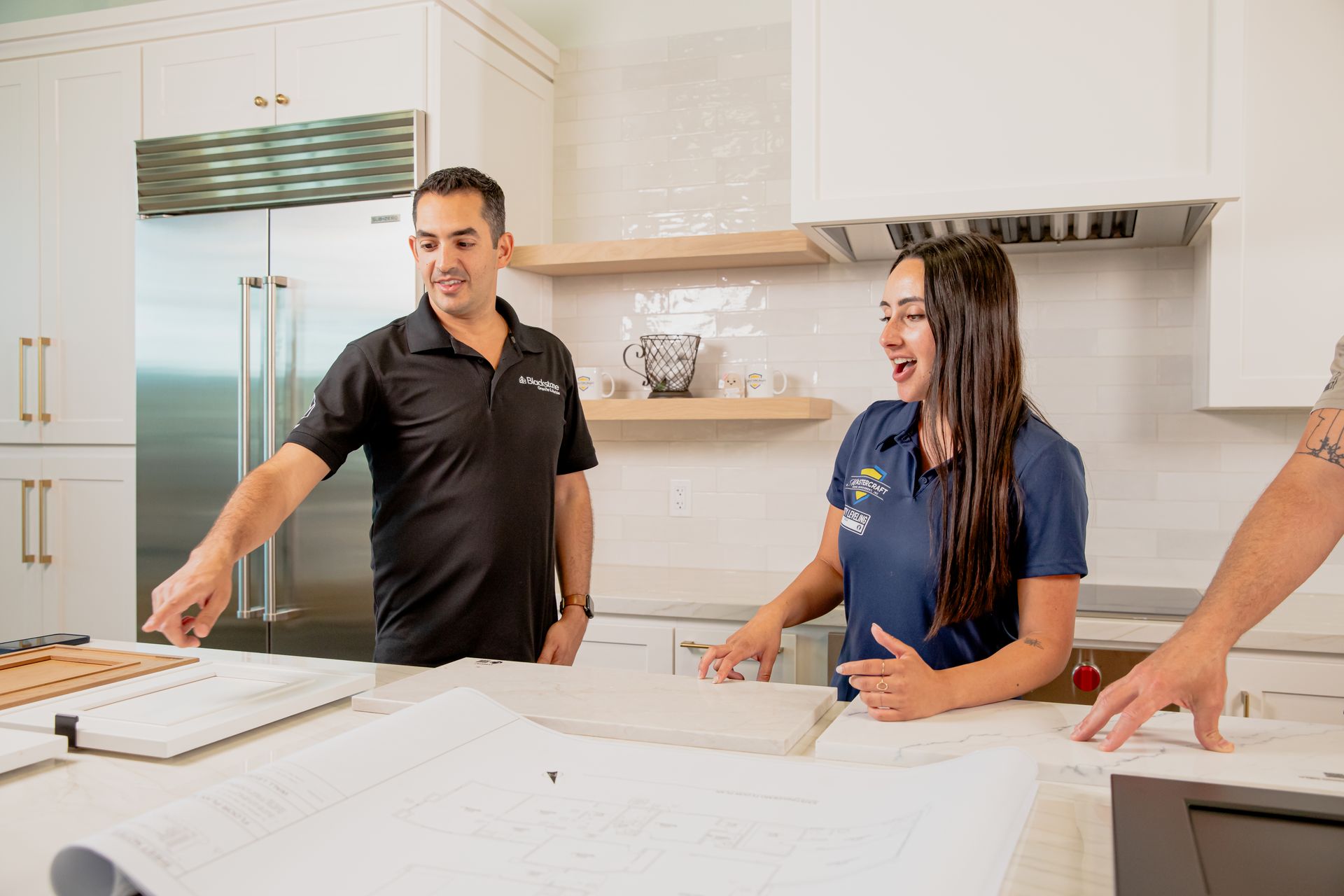 A man and a woman are standing in a kitchen looking at a blueprint.