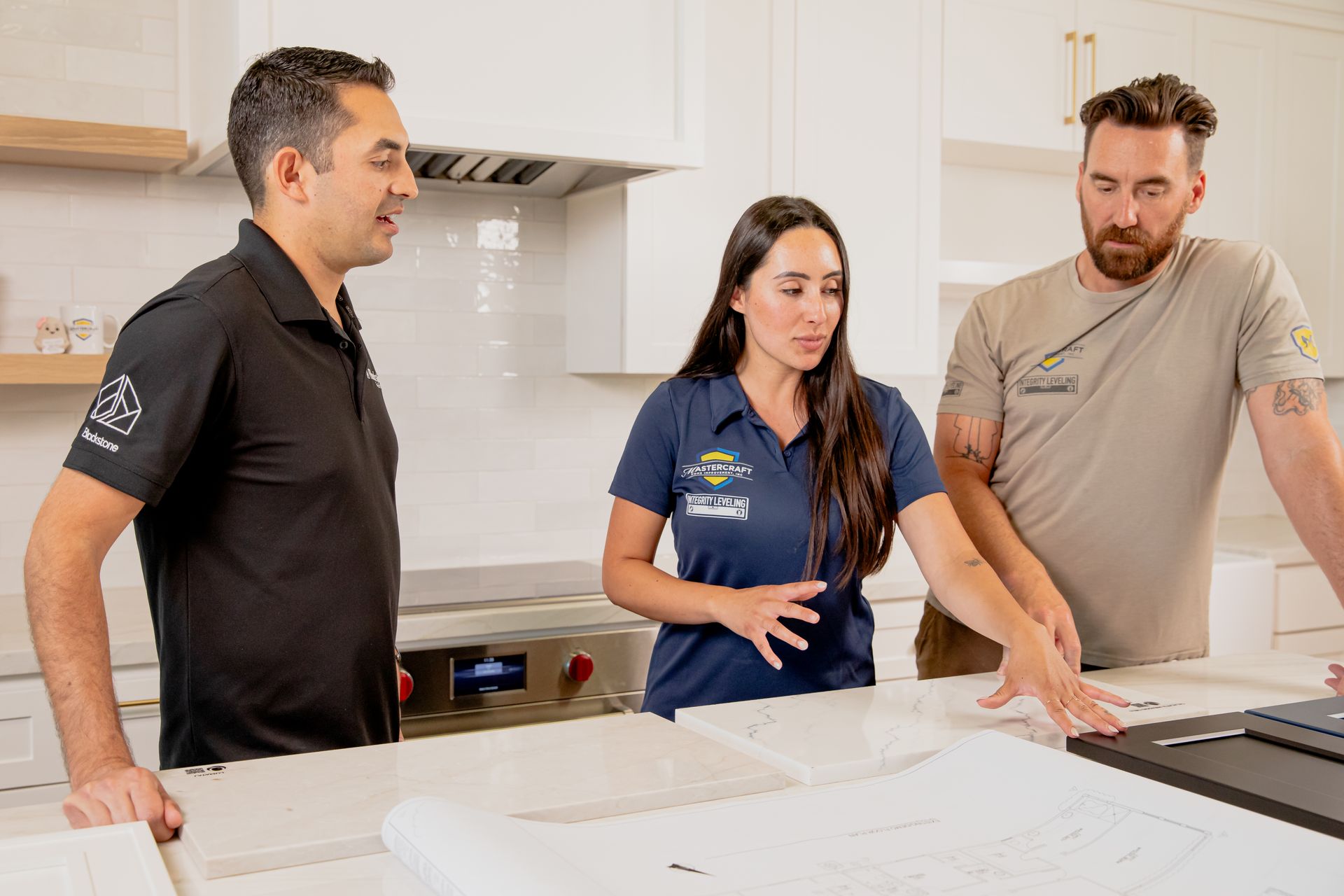 A group of people are standing around a kitchen counter looking at a blueprint.