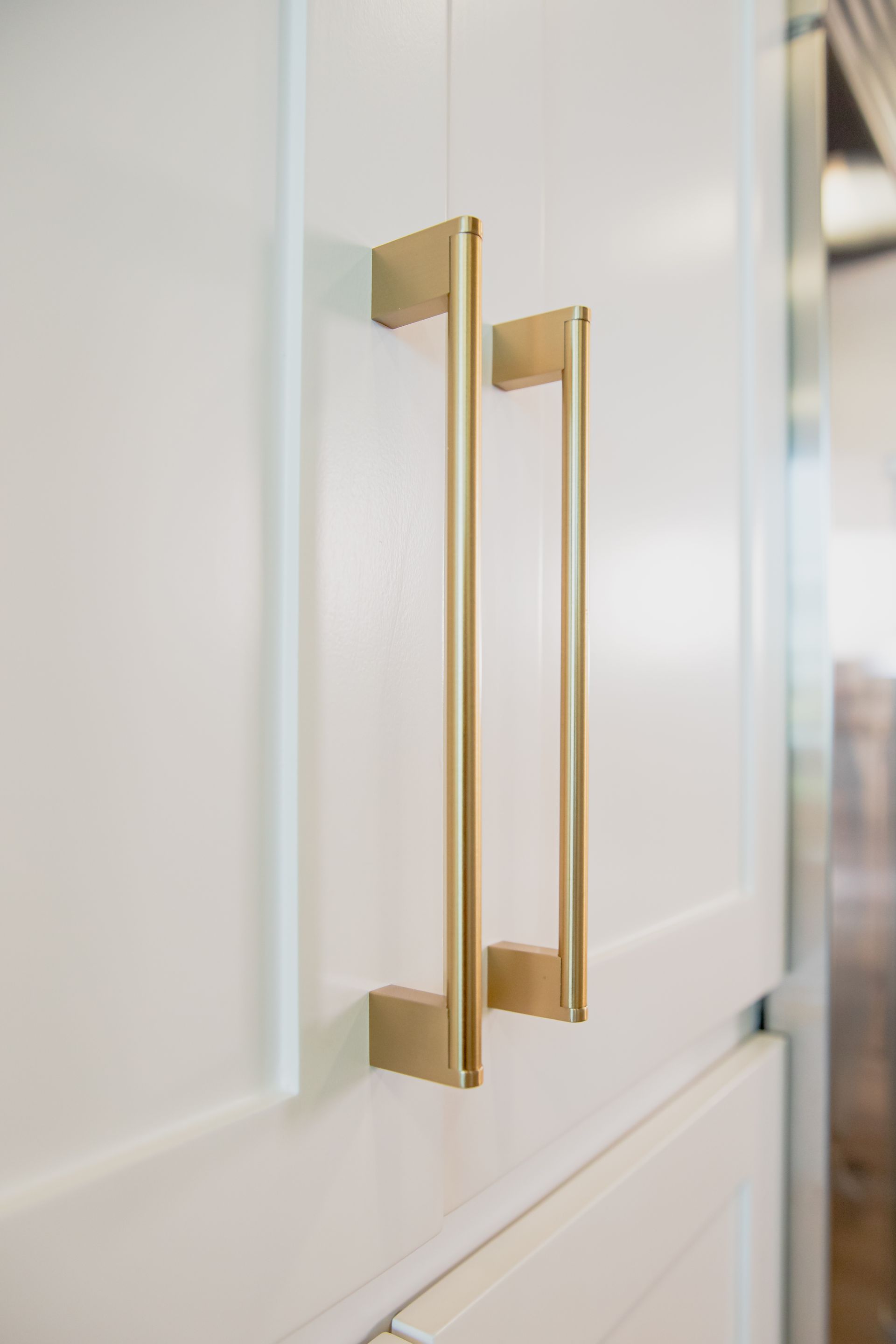 A close up of a brass handle on a white cabinet in a kitchen.