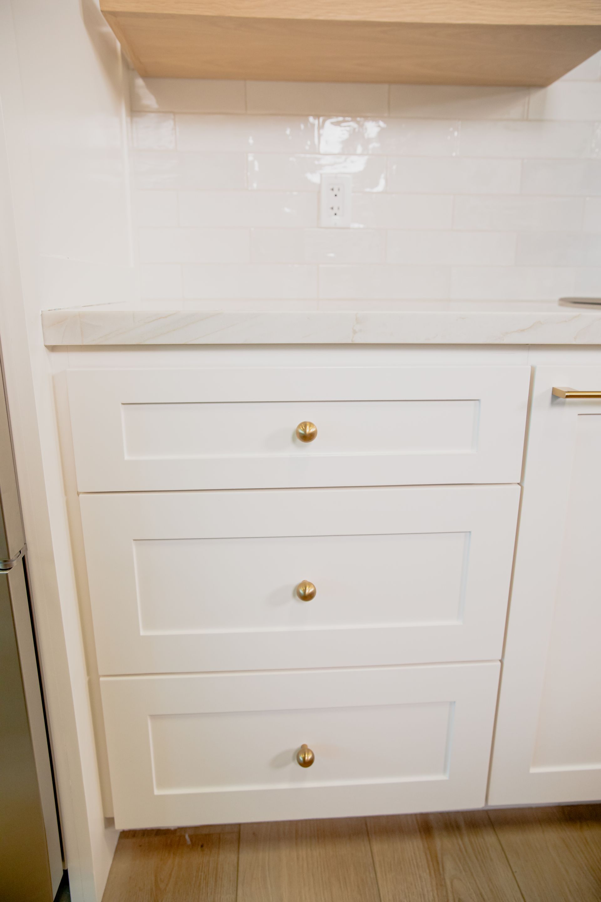 A kitchen with white cabinets and gold handles and drawers.