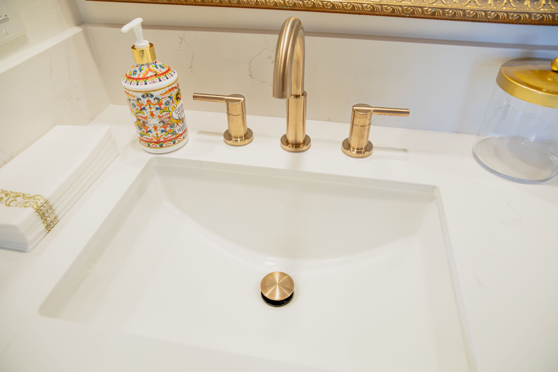 A bathroom sink with a gold faucet and a soap dispenser.