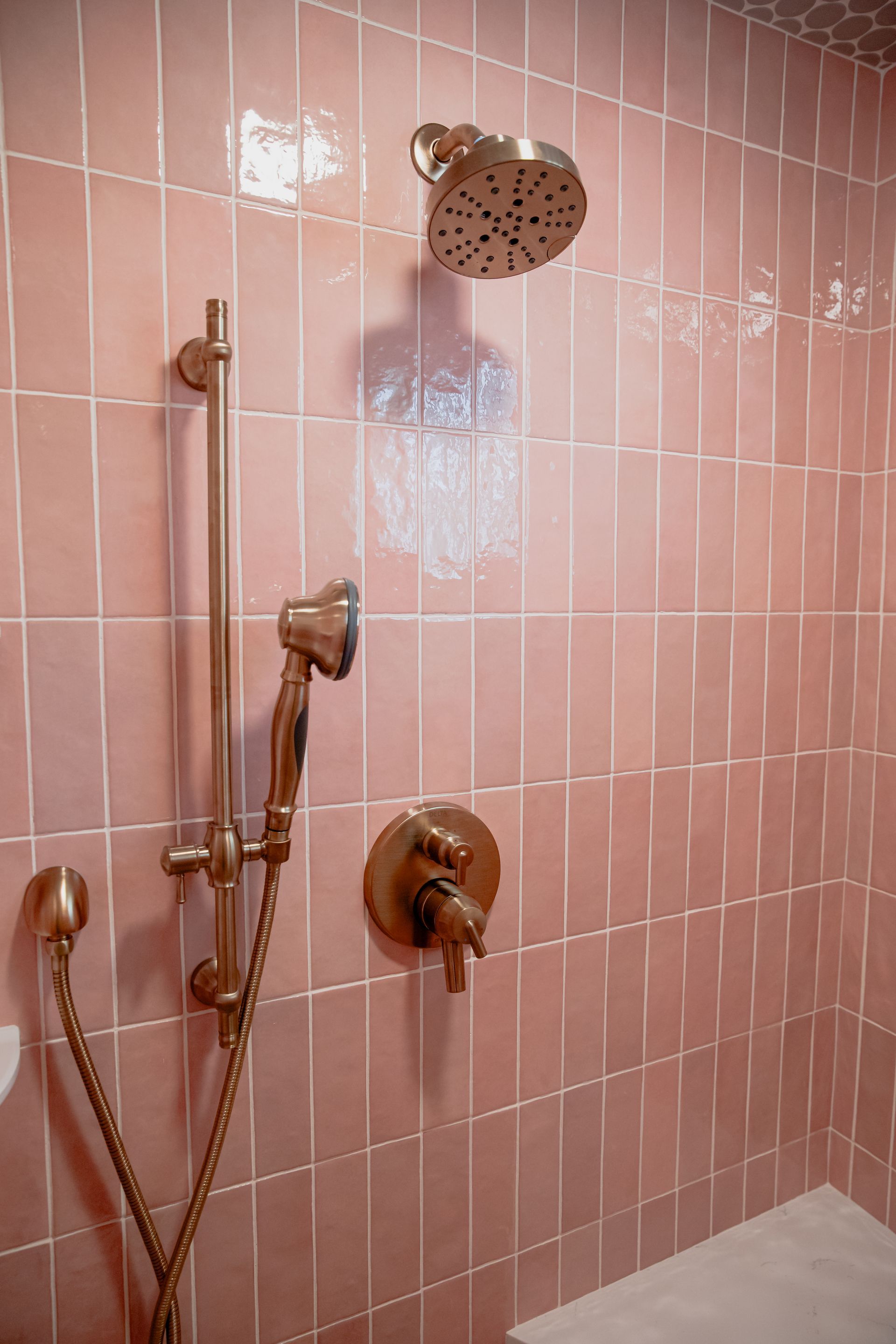 A close up of a shower head in a bathroom with pink tiles.