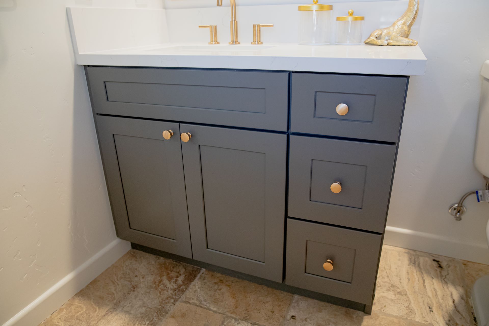 A bathroom vanity with gray cabinets and drawers next to a toilet.