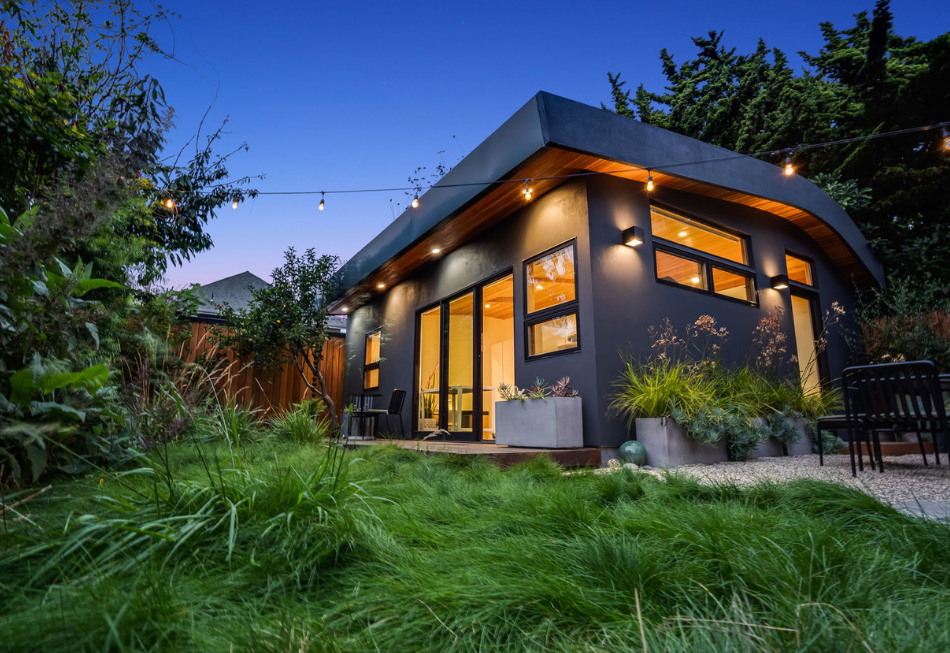 A small house with a lot of windows is sitting on top of a lush green field.