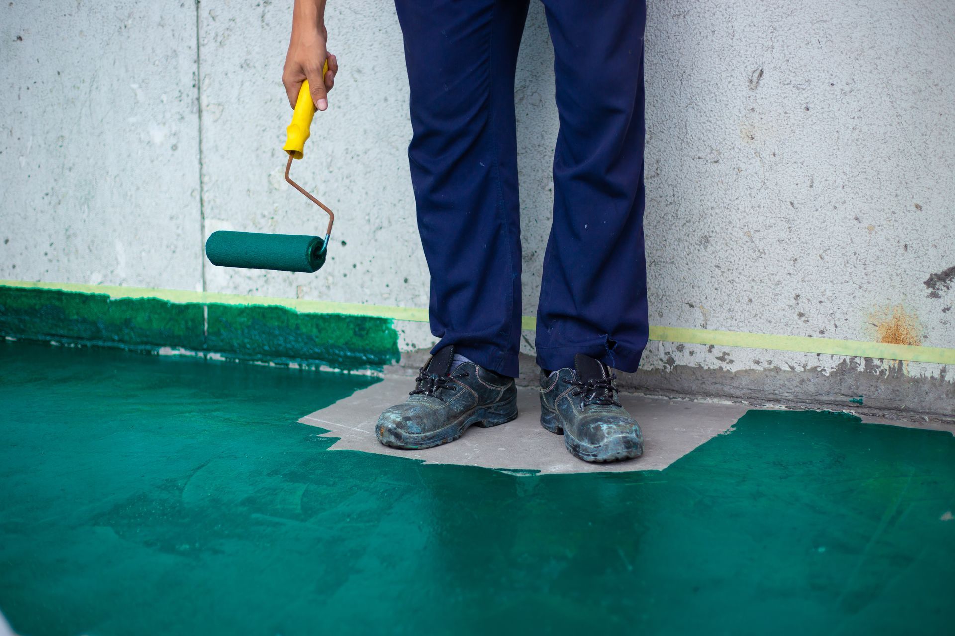 A man is painting a floor with a paint roller.