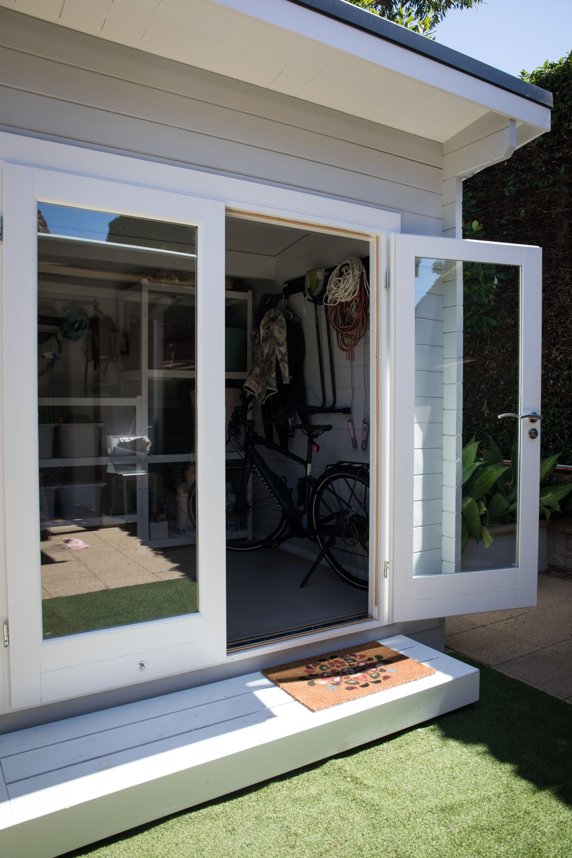 A white shed with the doors open and a bicycle inside.