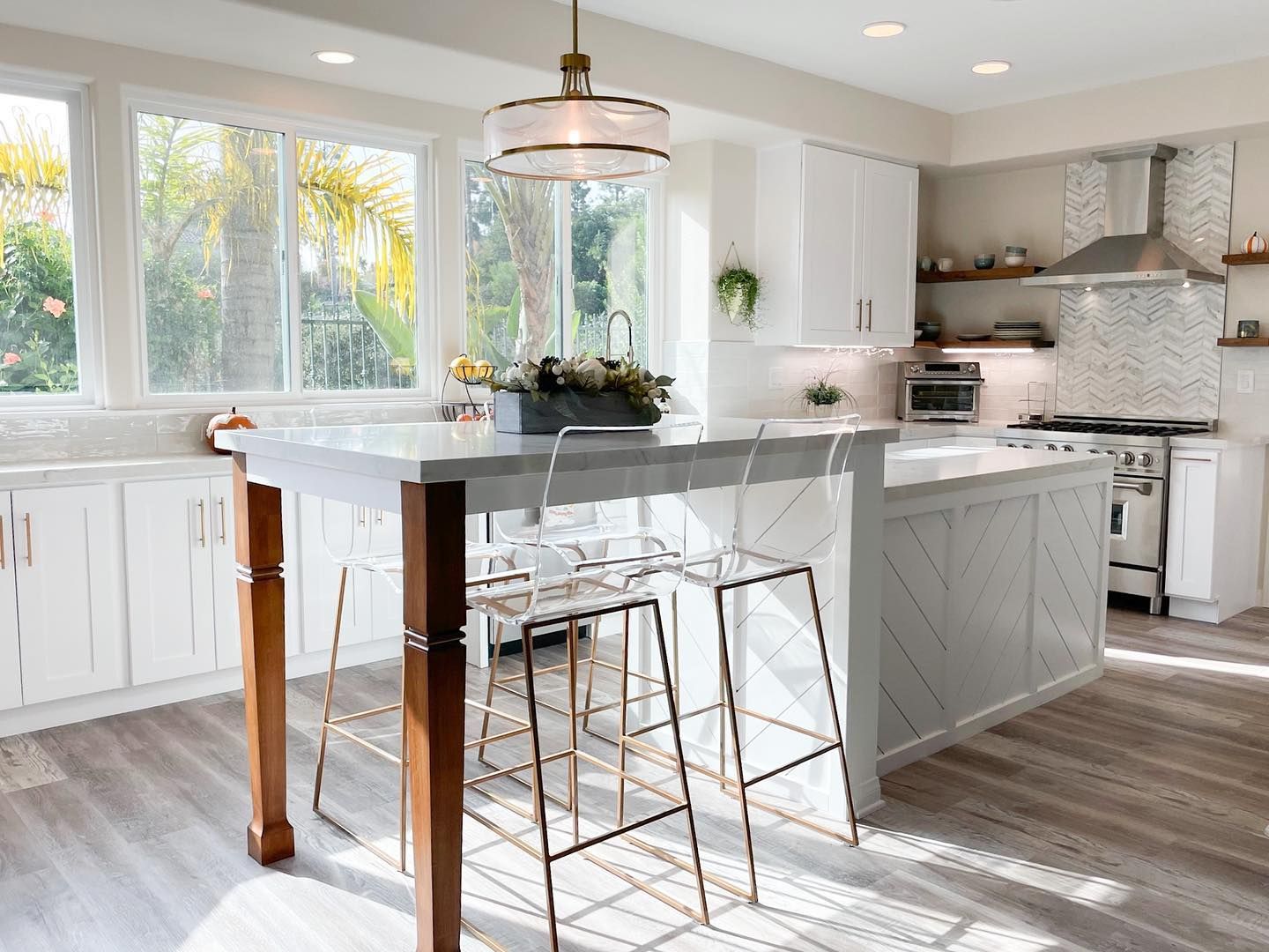 A kitchen with white cabinets , a large island , stools and a stove.