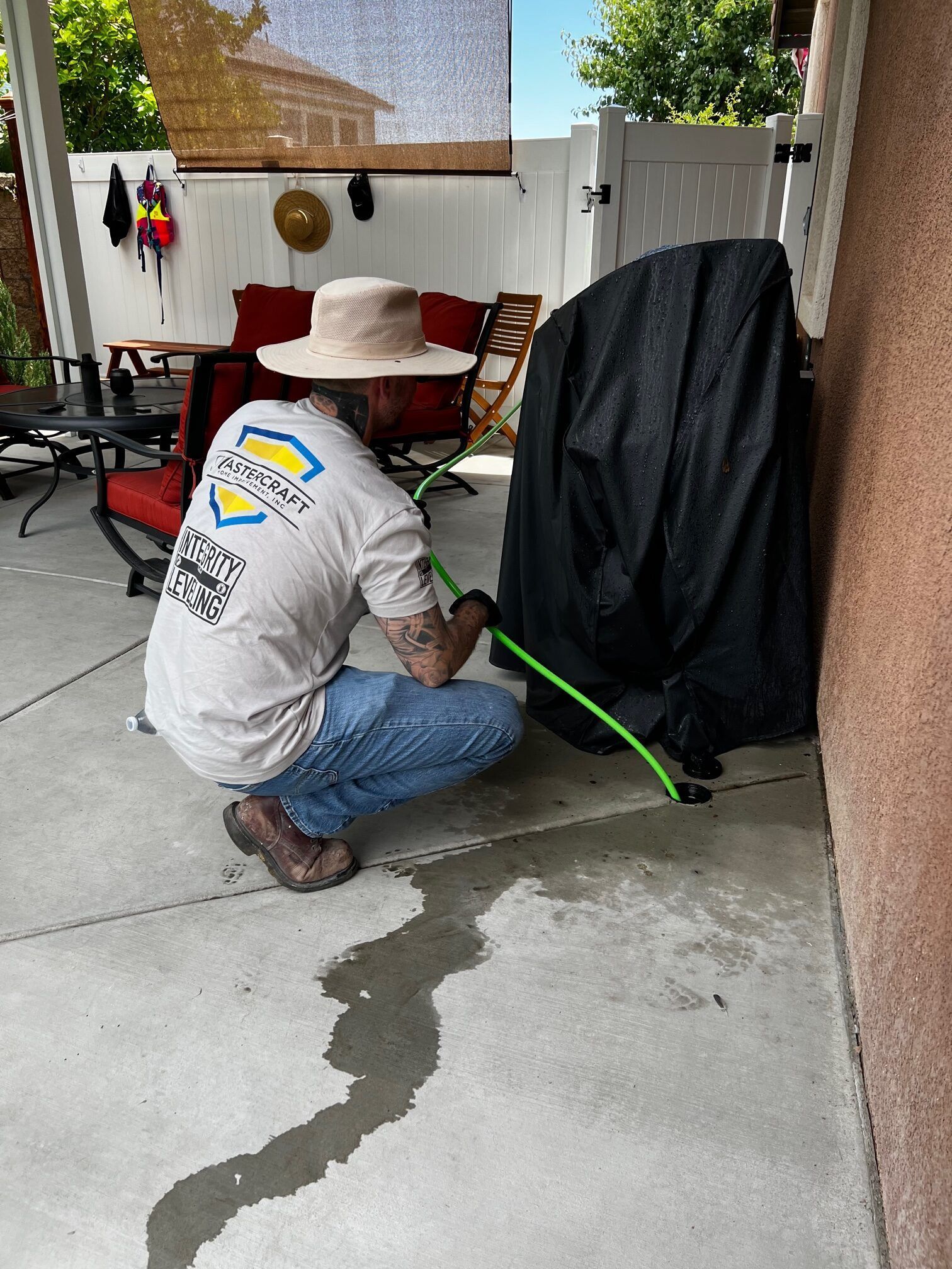 A man is kneeling down on a patio holding a green hose.