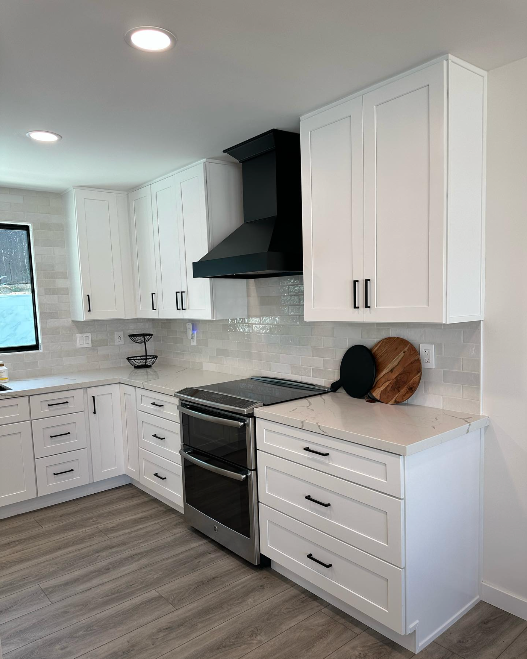 A kitchen with white cabinets , a stove , and a window.