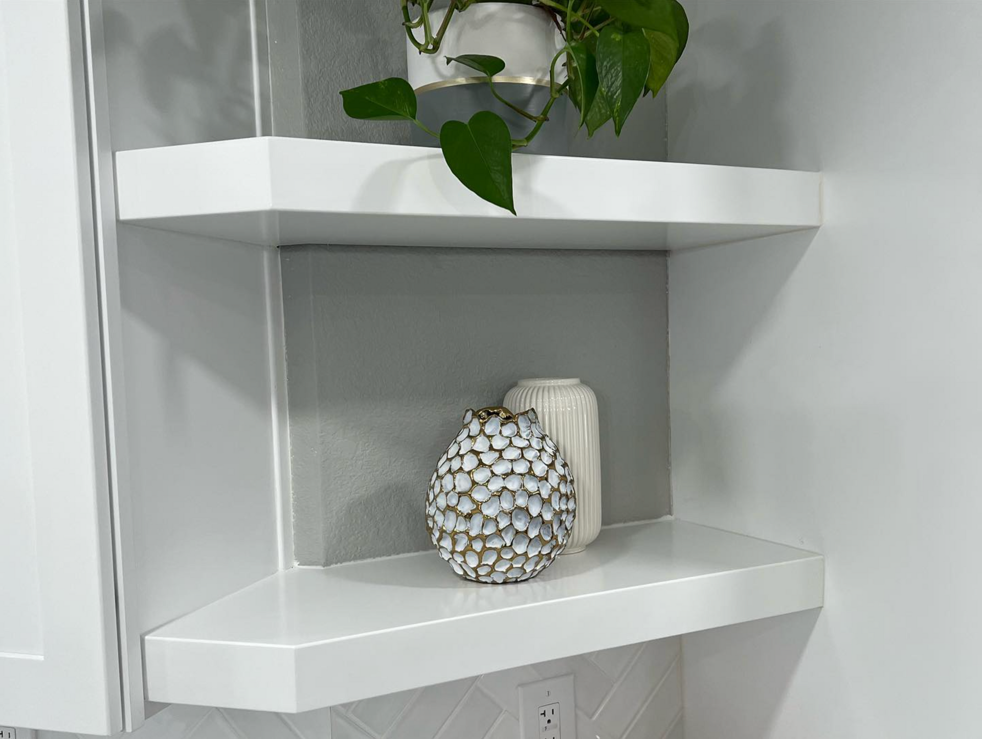 A white shelf with a vase and a plant on it.