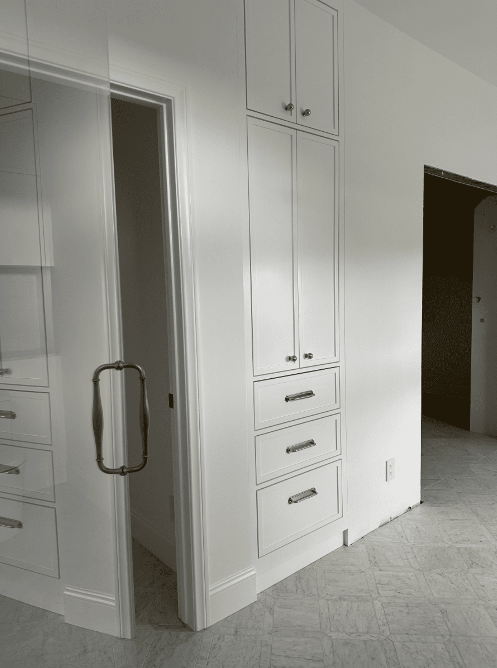 A black and white photo of a walk in closet with white cabinets and drawers.