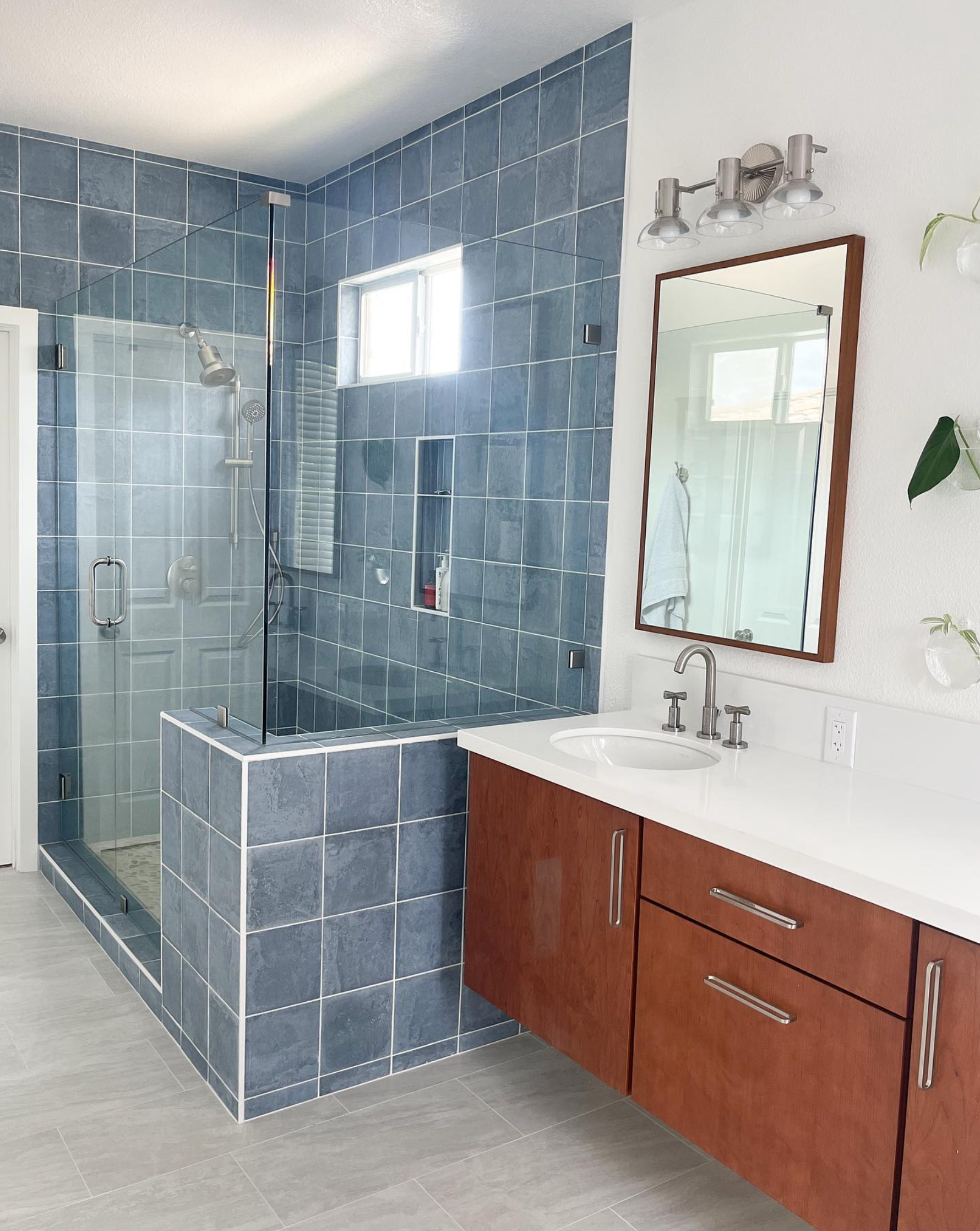 A bathroom with blue tiles , a sink , a mirror and a walk in shower.