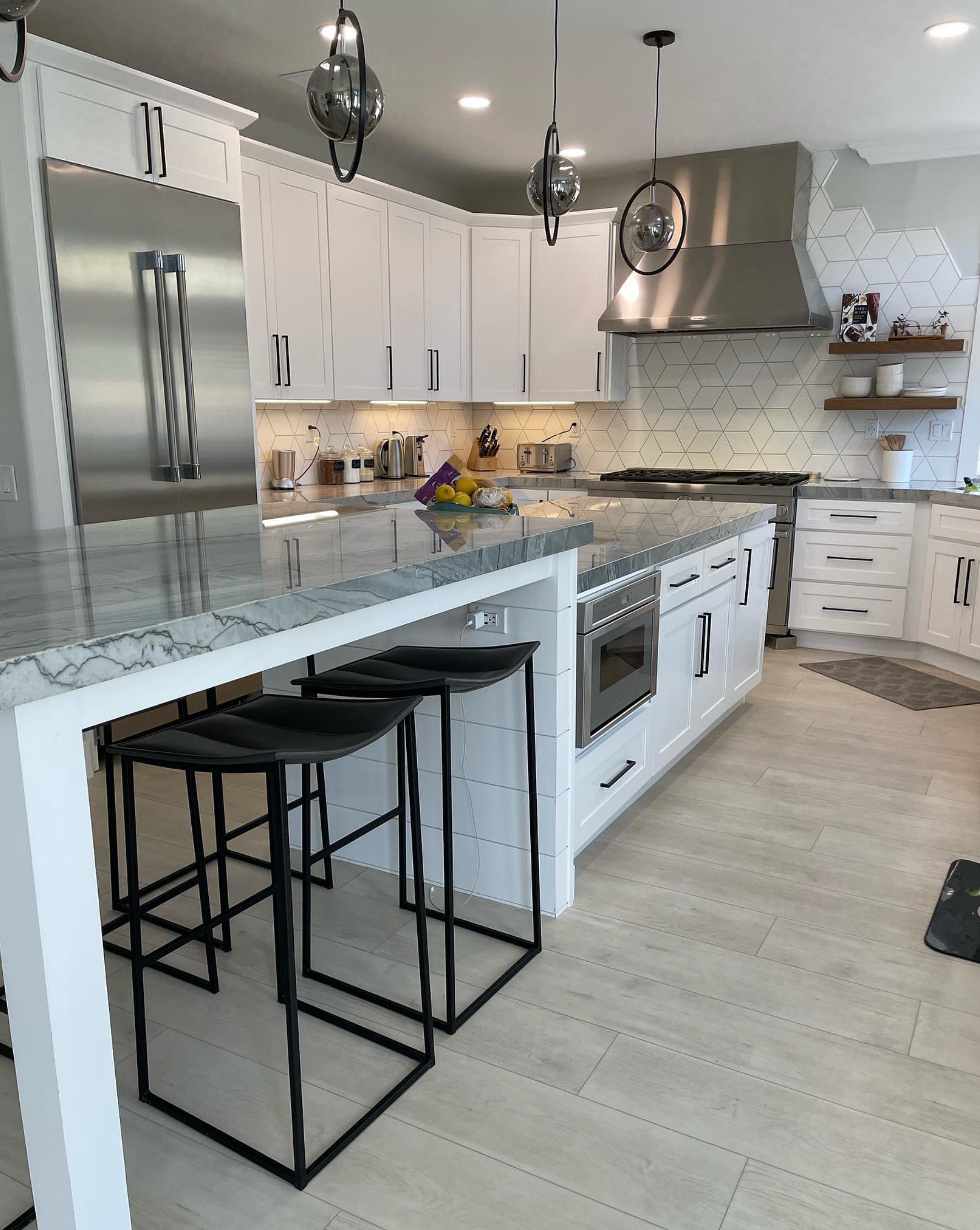 A kitchen with white cabinets , stainless steel appliances , and a large island with stools.