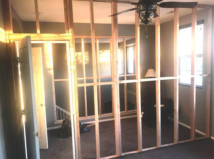 A room with a ceiling fan and a wall that is being built.