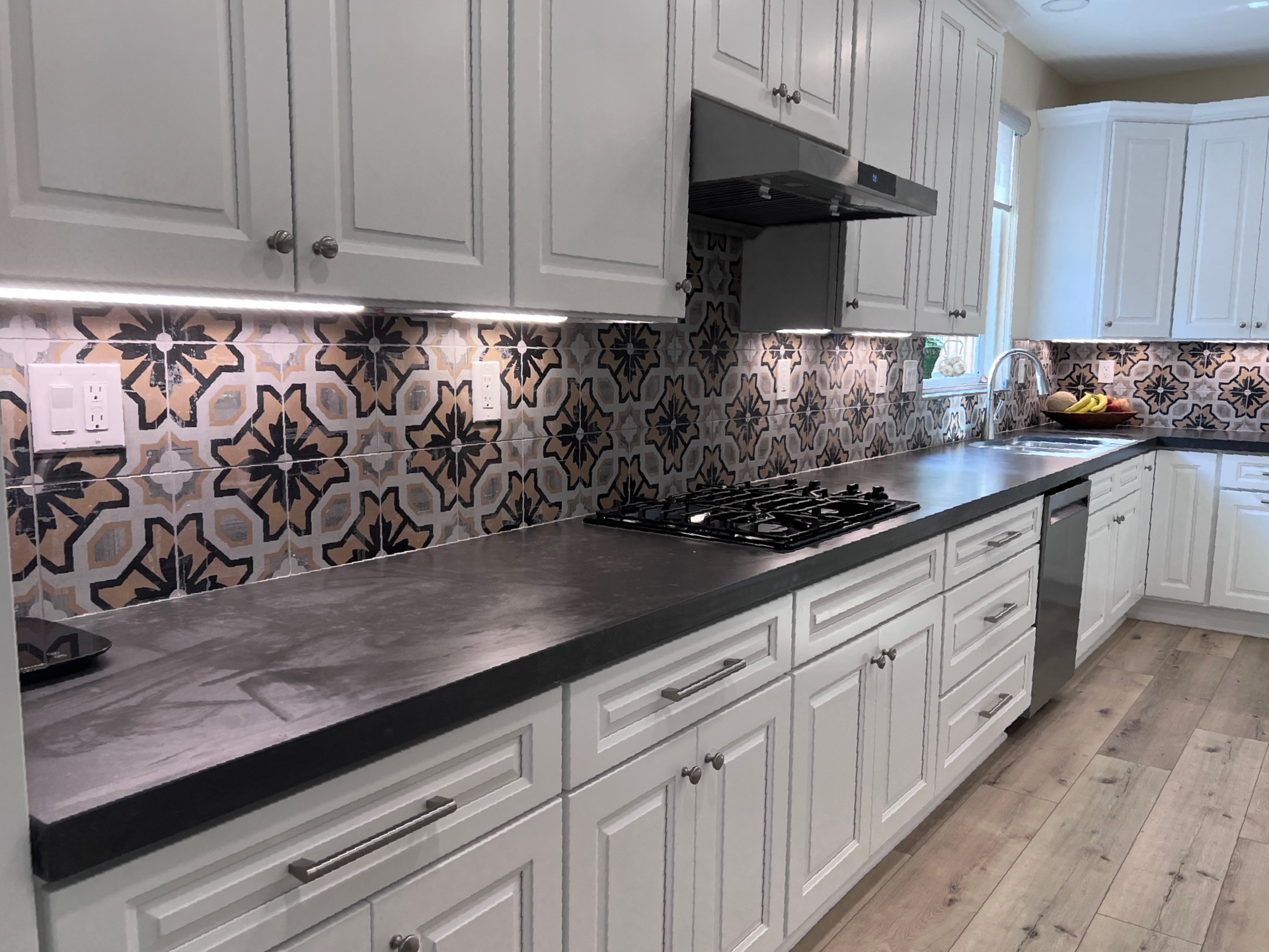 A kitchen with white cabinets , black counter tops , and a stove top oven.