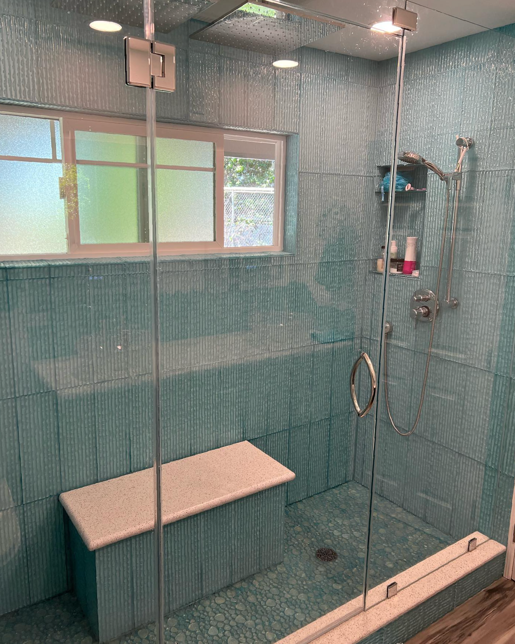 A bathroom with a walk in shower with a bench and a window.