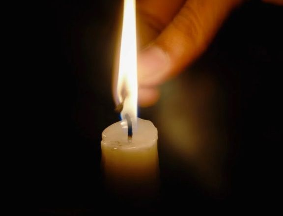 Hand lighting a candle in a dark setting for funeral homes in Port Washington, WI.