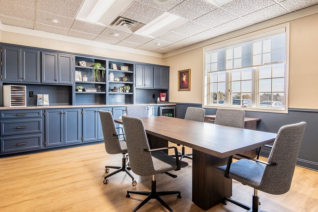 Conference room with a wooden table, blue cabinets, and large window. Chairs are arranged around the table.