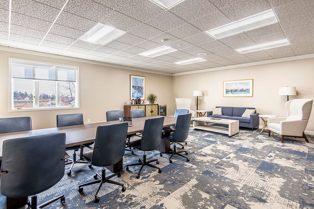 A modern office conference room with a long table, blue carpet, and a sitting area.