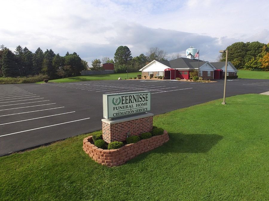 Sign for Ferness Funeral Home in front of a brick building and a parking lot. Green grass and trees are in the background.