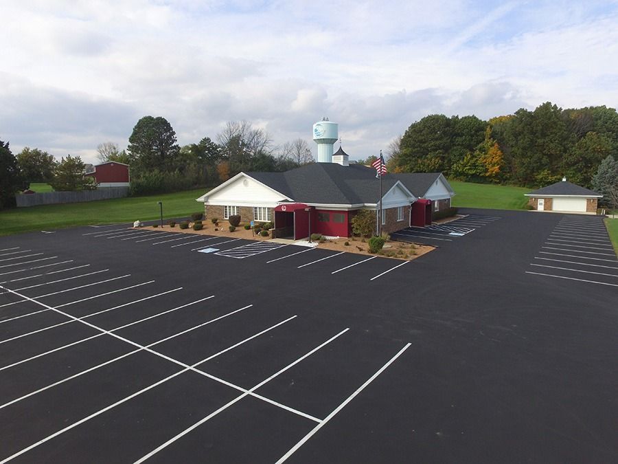 Aerial view of a business with a large empty parking lot and a water tower in the background. The building has red accents.
