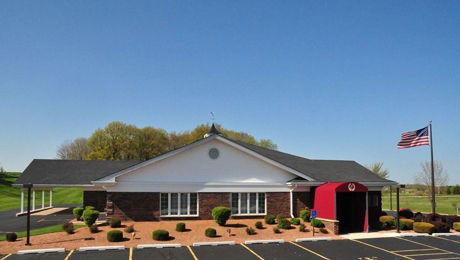 A low, brick building with a white gable roof and red accents. An American flag flies in the sun.