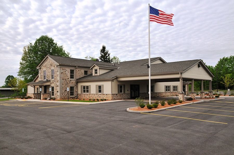 Exterior view of a building with an American flag. The building has light siding, a stone facade, and a covered porch.
