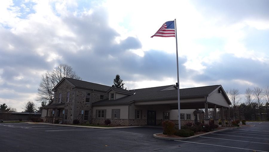 A stone building with an American flag in front; cloudy sky above a parking lot.