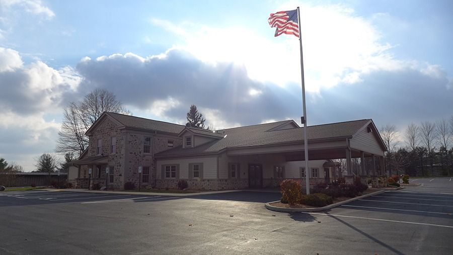 Stone building with an American flag waving in the sunlight; parking lot in front.