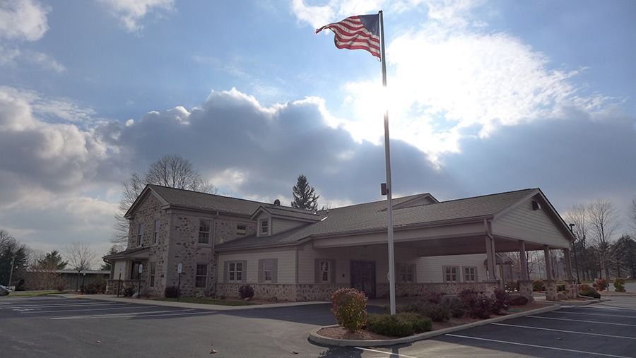 A stone building with a long covered porch; an American flag flies high under a bright sky.