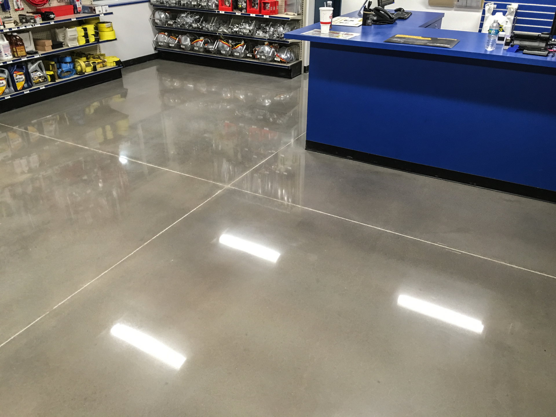 Retail store interior with shiny gray floor, stocked shelves, and a blue counter on the right.