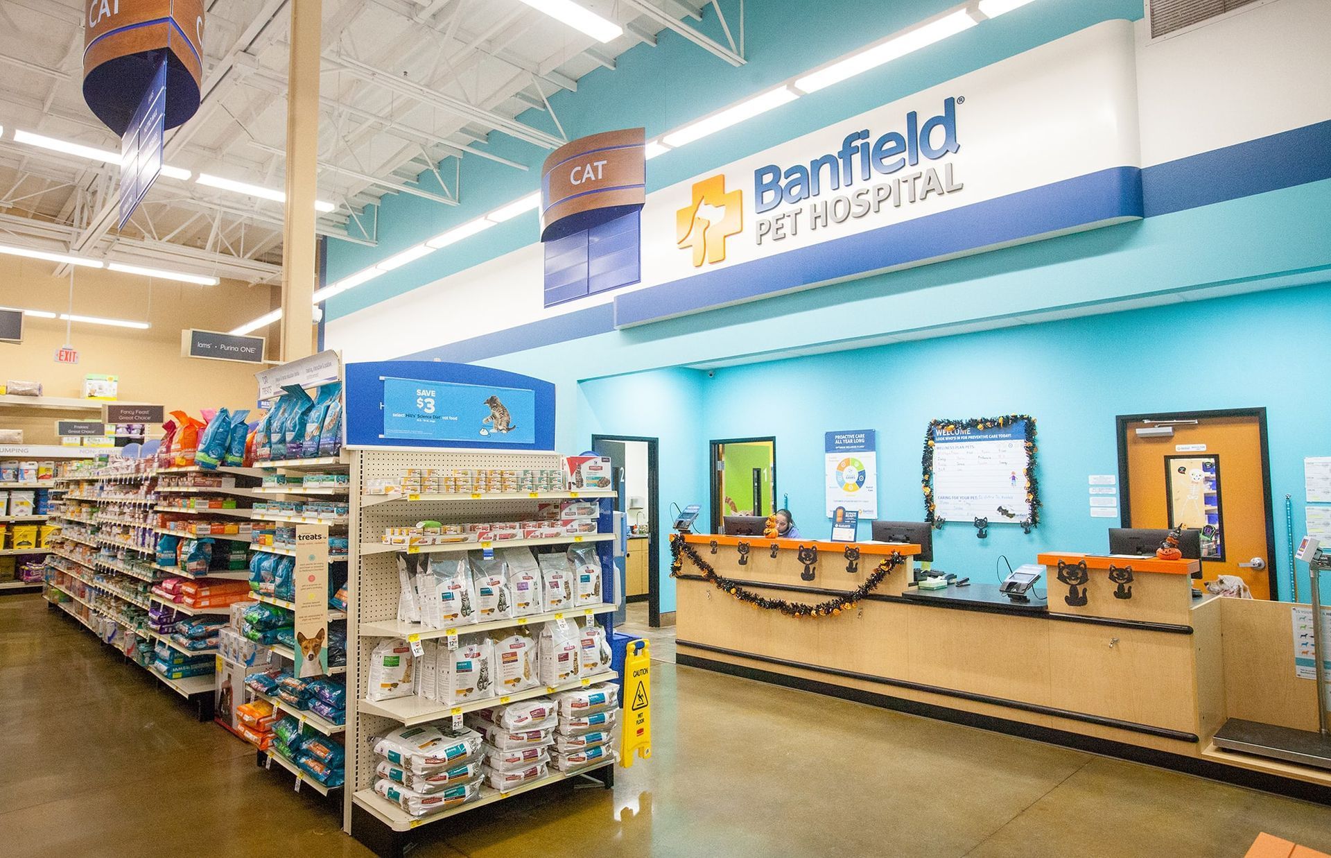 Retail pharmacy checkout area with shelves of medicines and a blue “Riverfield Pet Hospital” sign