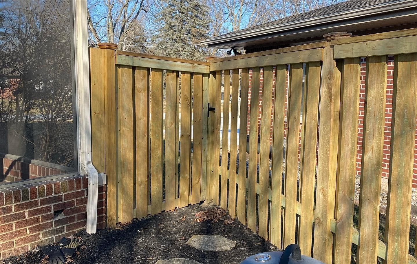 Wooden fence with gate against a brick wall; a downspout is visible.