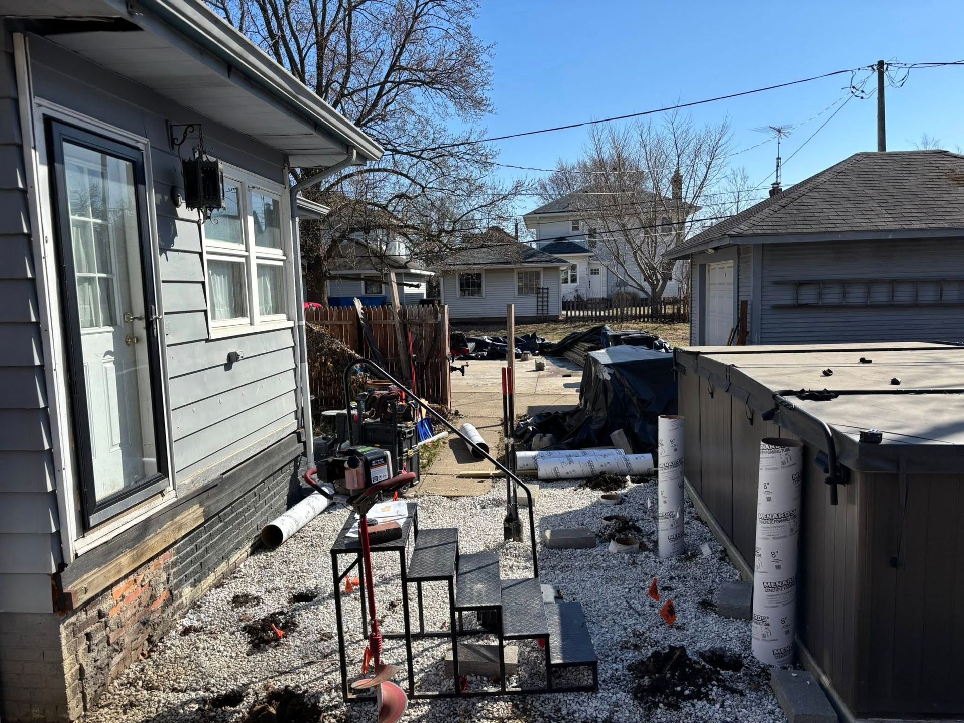 Backyard with construction materials; gray house, hot tub, steps, and white gravel.