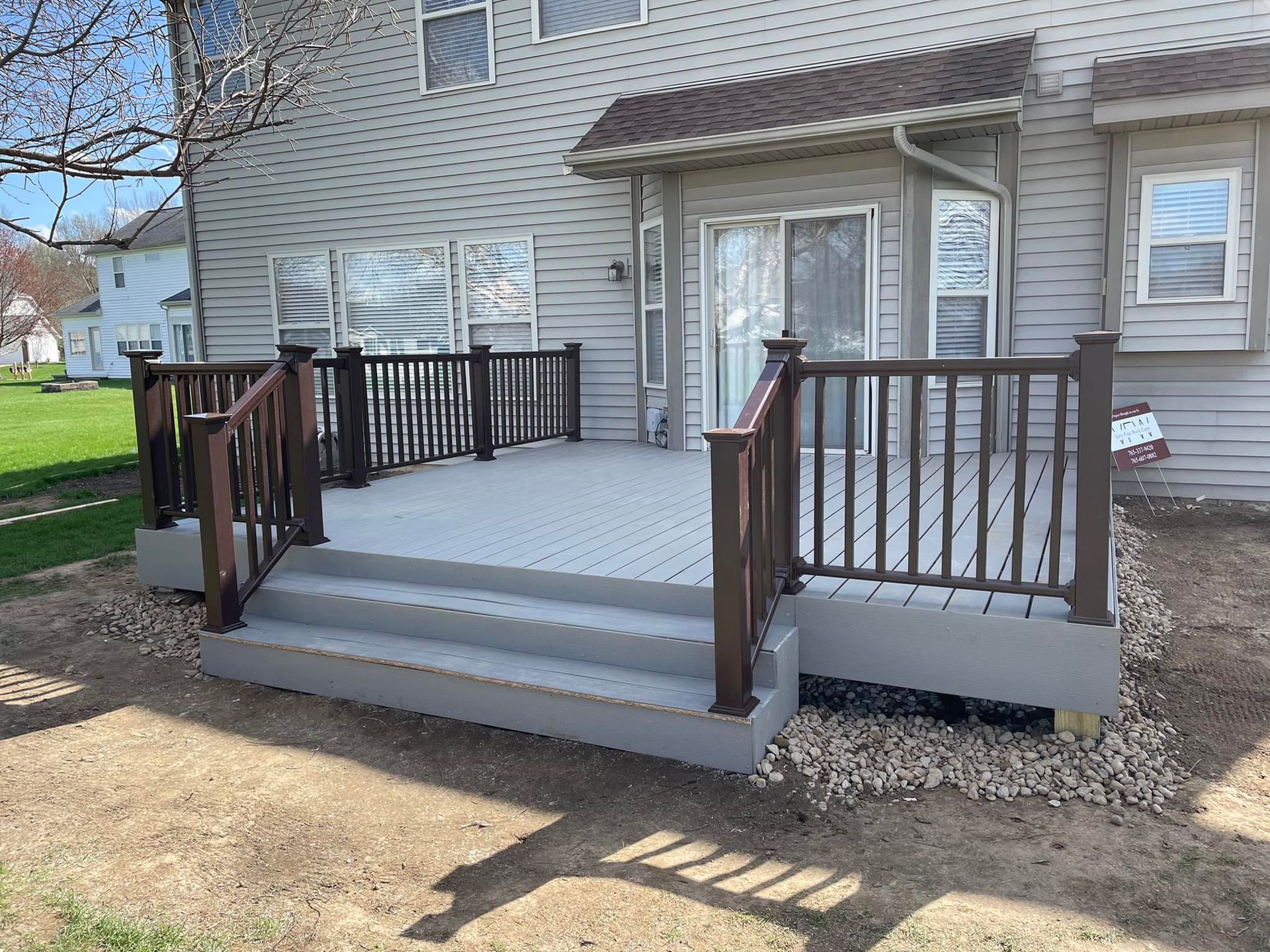 A composite deck with gray decking, brown railings, and stairs leading to a house with gray siding.