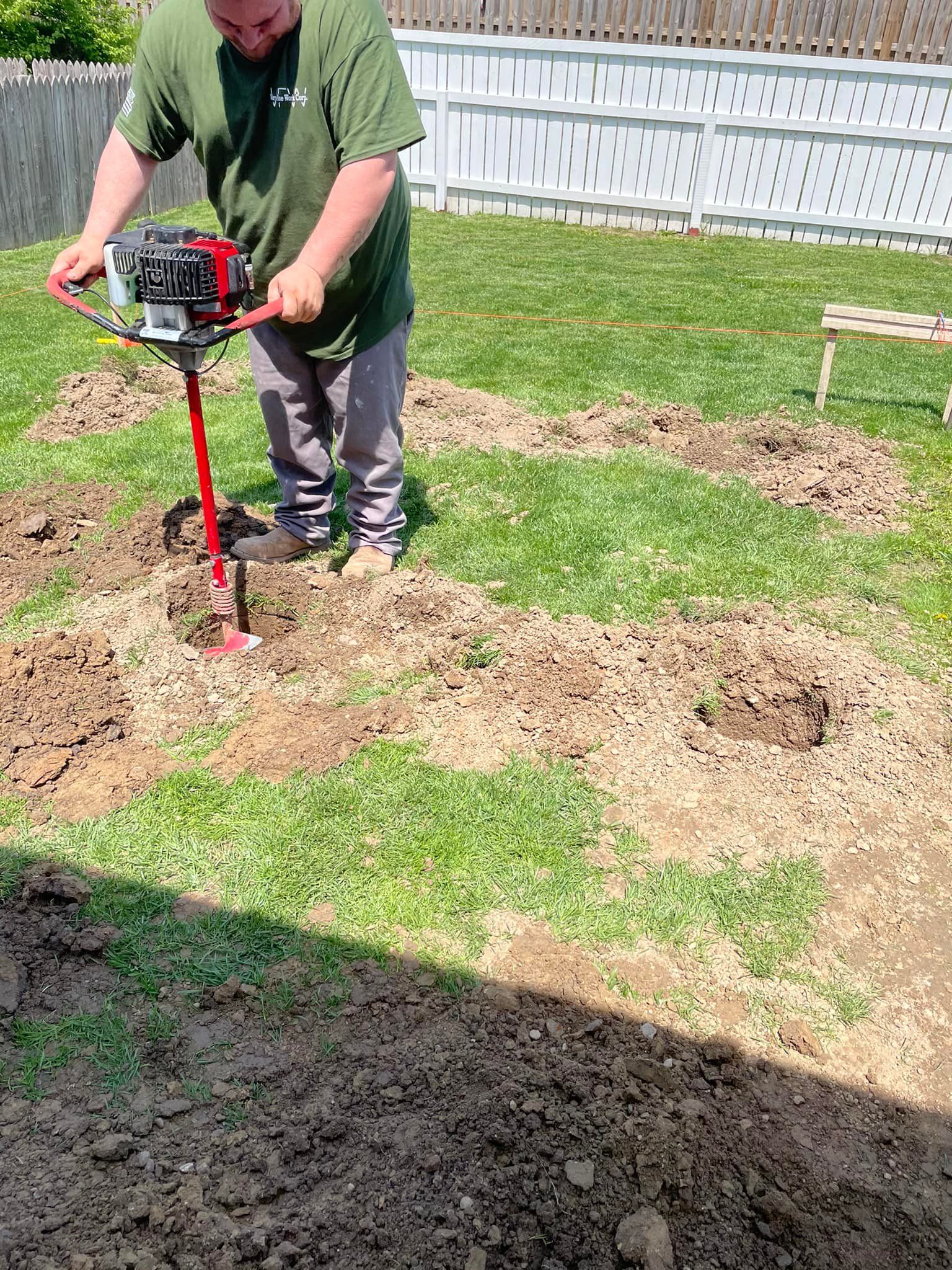 Man using a red auger to dig holes in a grassy yard for a fence.