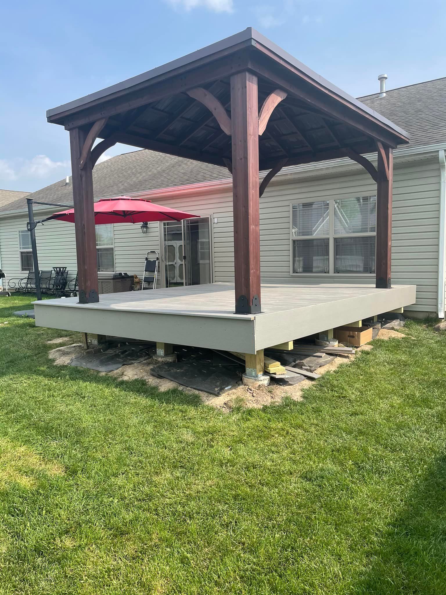 Deck with a brown gazebo in a backyard. Green grass surrounds it. Light siding on the house.