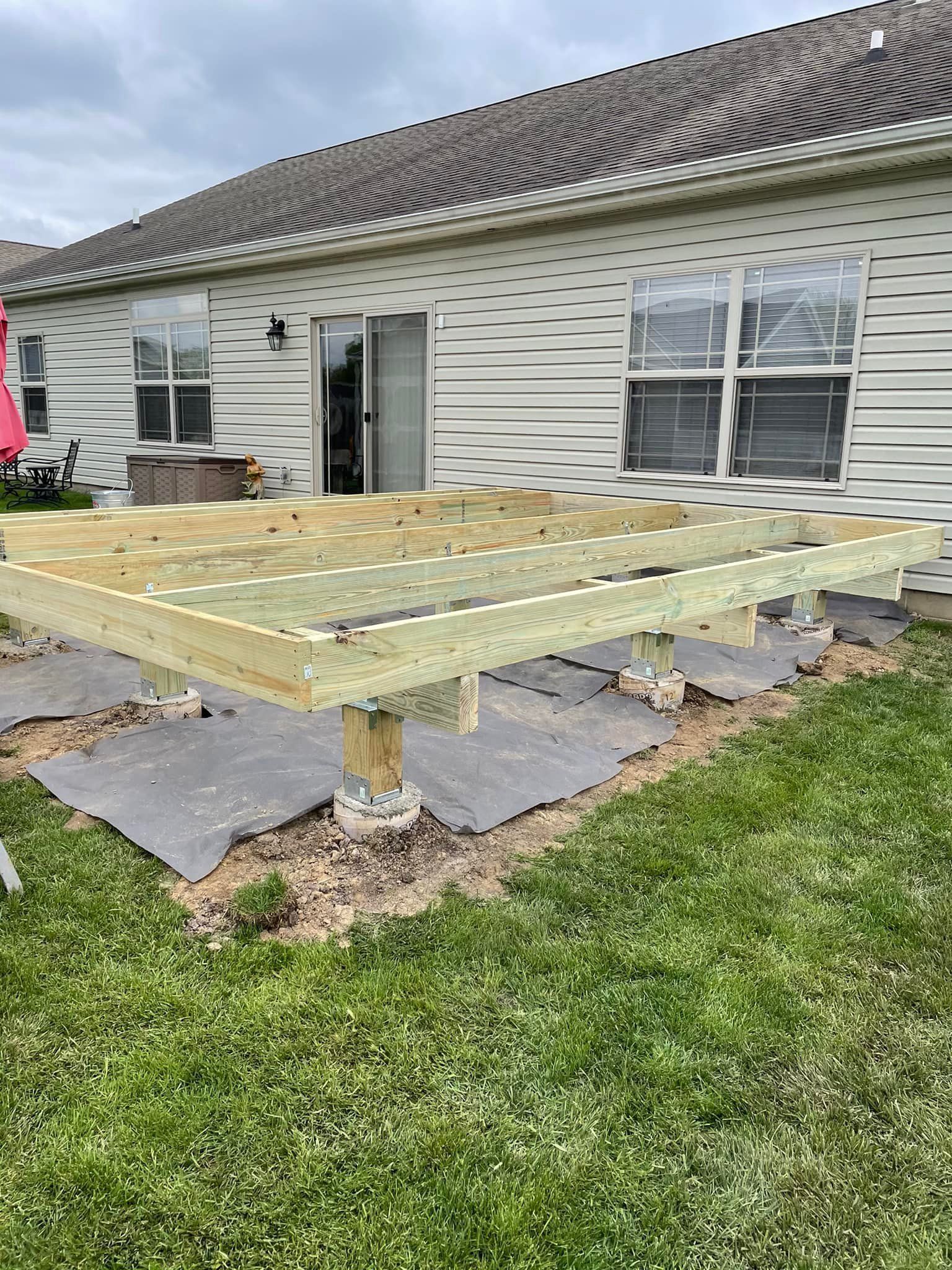 A partially built wooden deck on concrete blocks in a backyard next to a house.
