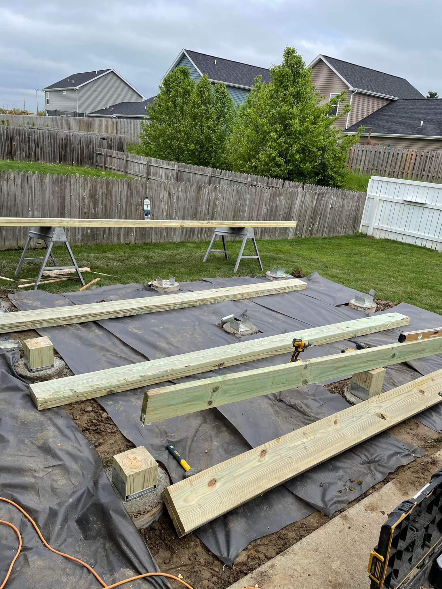 Deck construction: Wooden beams and posts on black tarp in backyard.